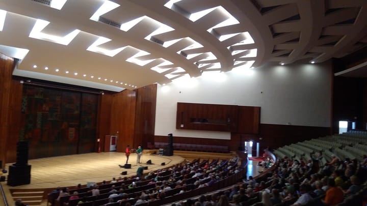 The Aula Magna auditorium at the University of Lisbon rectory, a large sloping hall of green seats filled with an audience facing a wooden stage