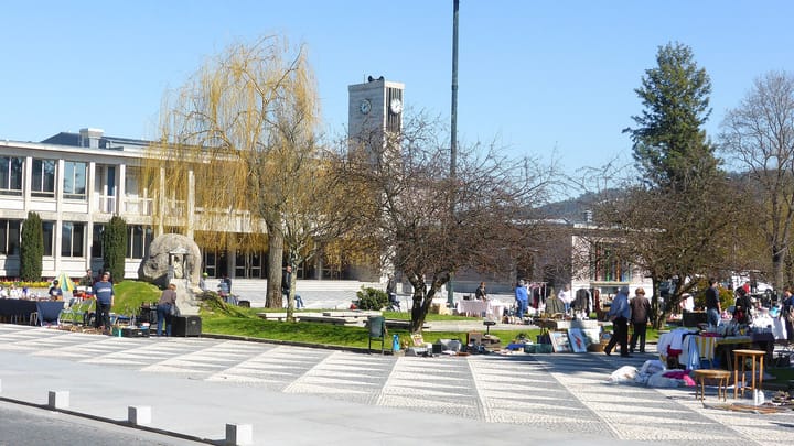 The main square in Santo Tirso on a market day, with stalls laid out on the calcada paving and the town hall clock tower behind the trees.
