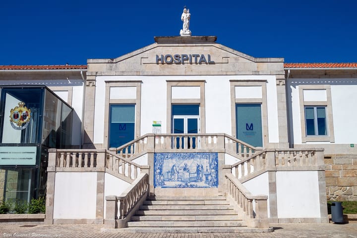 Facade of a Portuguese public hospital with the word HOSPITAL, a stone staircase and an azulejo tile panel