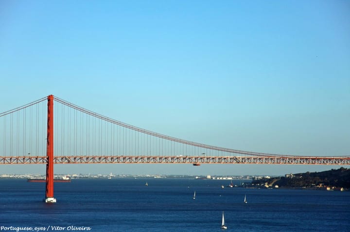 The red steel Ponte 25 de Abril suspension bridge spanning the Tagus river in Lisbon, with sailboats below