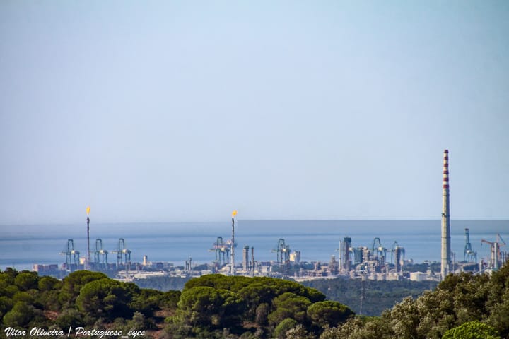 The Sines oil refinery on the Portuguese coast, with flare stacks and a tall chimney rising above pine woodland