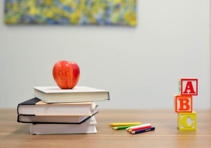 A stack of books with a red apple on top and alphabet blocks spelling ABC on a classroom table, representing special education