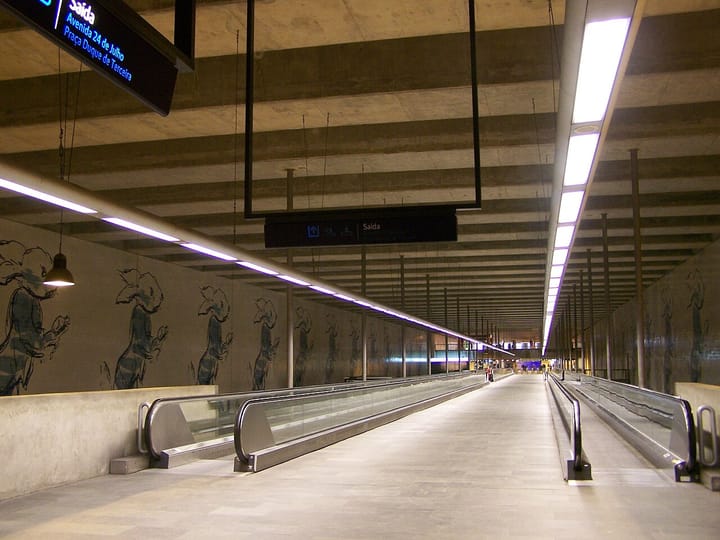 The long underground concourse at Cais do Sodre metro station in Lisbon, with parallel moving walkways, a lit ceiling strip and Saida signs for Avenida 24 de Julho and Praca Duque de Terceira