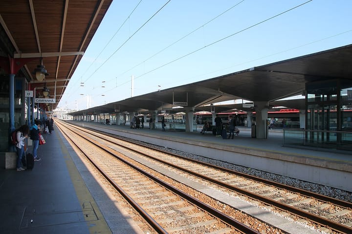 Platforms at Porto's Campanha railway station, with CP signage, overhead catenary and passengers waiting beside the tracks under a concrete canopy