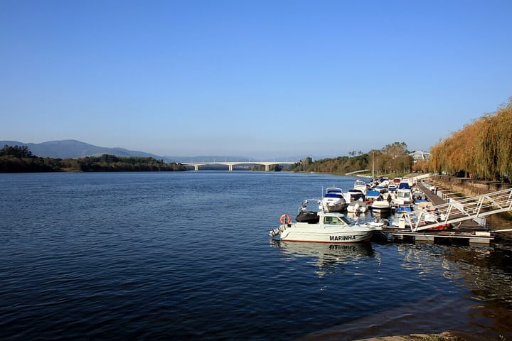 The Minho river at Vila Nova de Cerveira, with small boats and a Portuguese Navy launch moored at the town's pontoon and the international bridge to Galicia in the distance