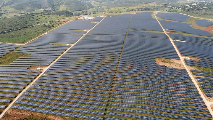 Aerial view of a utility-scale photovoltaic plant at Bensafrim, near Lagos in the Algarve, with long rows of blue solar panels covering rolling scrubland and dirt access tracks between them