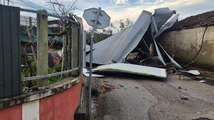 A corrugated metal roof torn off and dumped across a village street at Amor, Leiria, with broken roof tiles scattered on the tarmac after a winter storm in Portugal