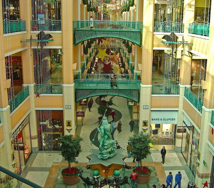 The multi-level interior atrium of a large Lisbon shopping centre with shopfronts, walkways and a central sculpture
