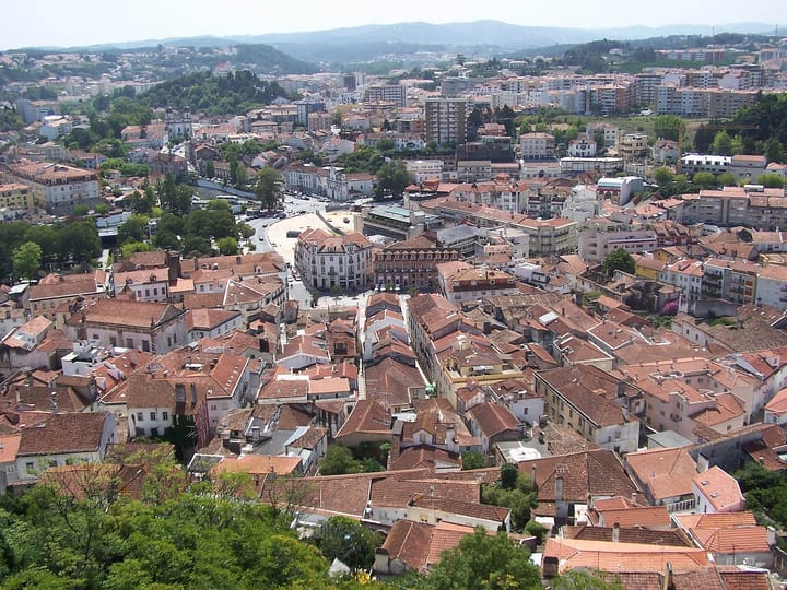 An aerial view of the Portuguese city of Leiria, with red-tiled rooftops stretching toward wooded hills