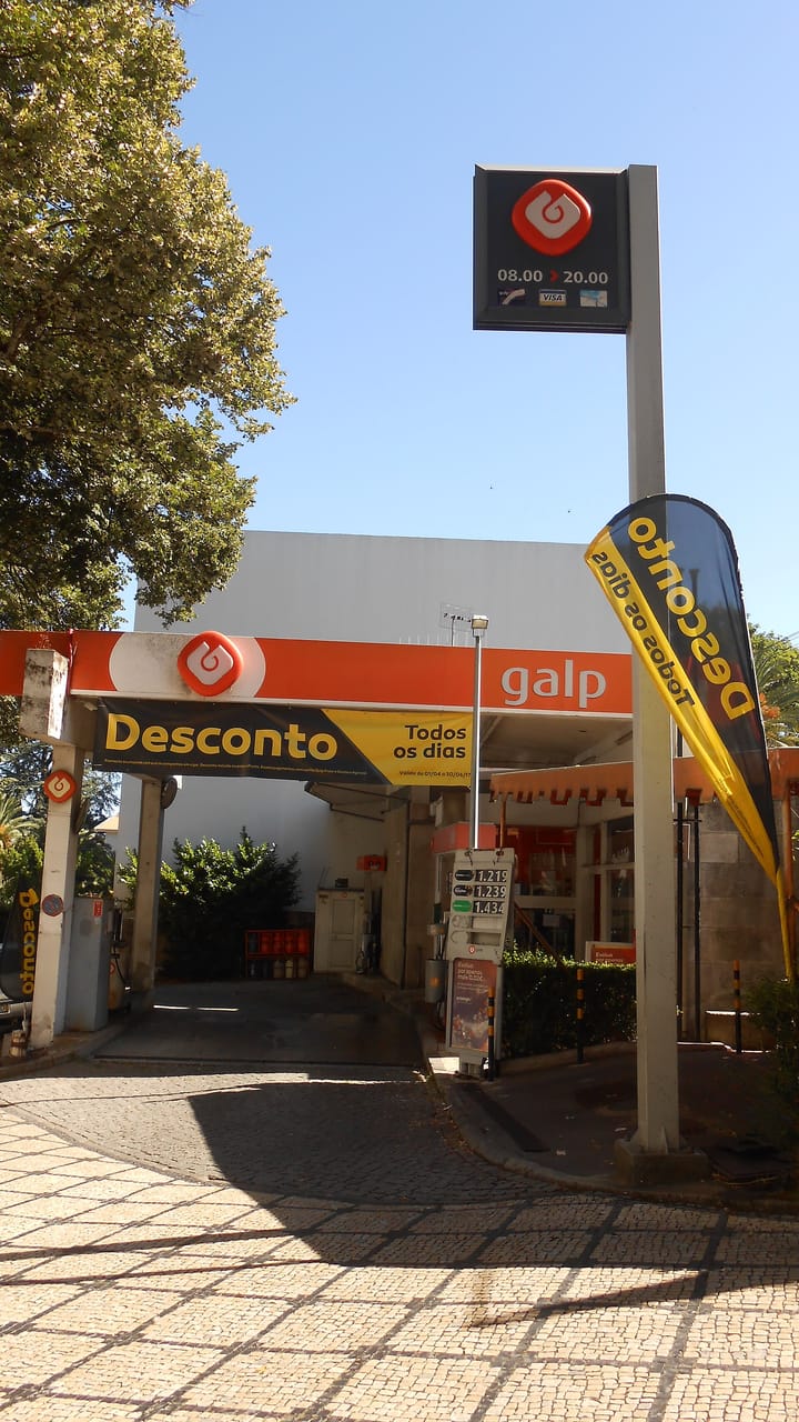 A Galp filling station in Portugal with the company's orange logo, a price display and a Desconto promotional banner under a blue sky