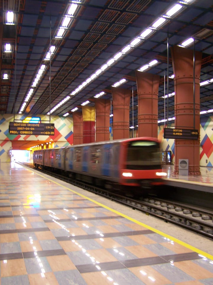 A red Lisbon Metro train arriving at the colourful, tiled platform of Olaias station