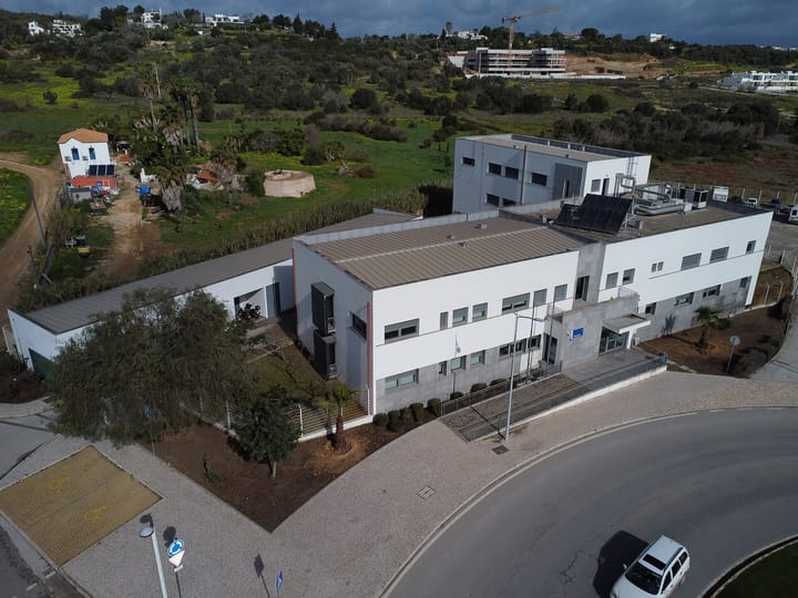 An aerial view of the PSP police station in Lagos in the Algarve, a long white two-storey building with a blue Policia sign above its entrance beside a roundabout.