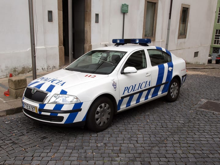 A white and blue PSP patrol car parked on granite cobbles at Largo Primeiro de Dezembro in Porto, with the word POLICIA along its bonnet and side.