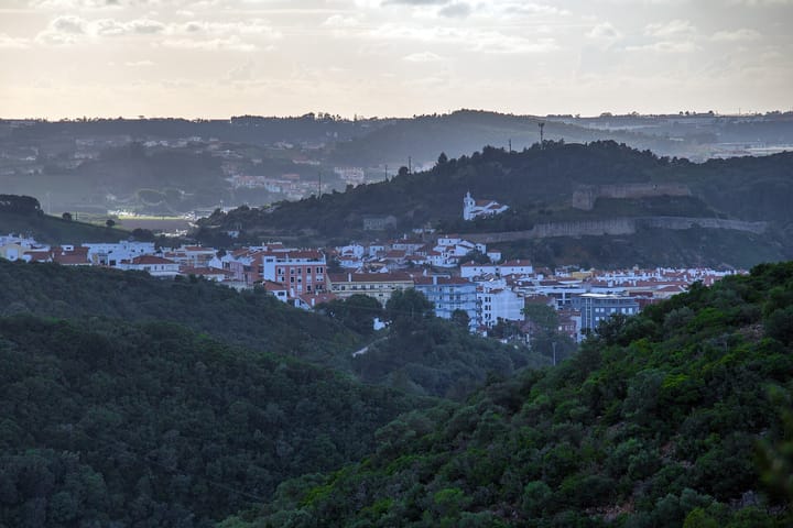 A view of the town of Torres Vedras in Portugal at dusk, white houses with red roofs below a hilltop medieval castle and church