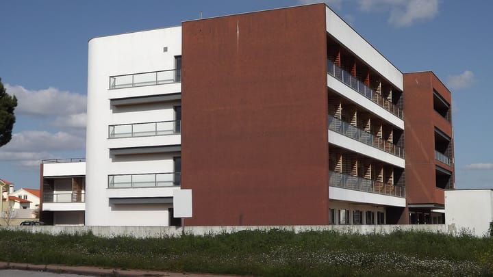 The exterior of a Portuguese integrated continuing care unit, a modern three-storey building in white render and red panels with shaded balconies.