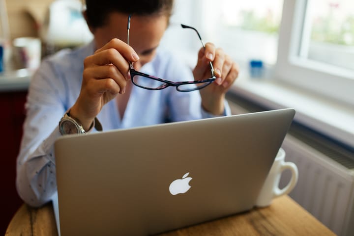 A young professional working on a laptop at a desk by a bright window with a coffee mug