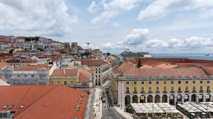 Rooftops of Lisbon's Baixa and the arcades of Praça do Comércio seen from the Rua Augusta arch, with the cathedral and the Tagus behind
