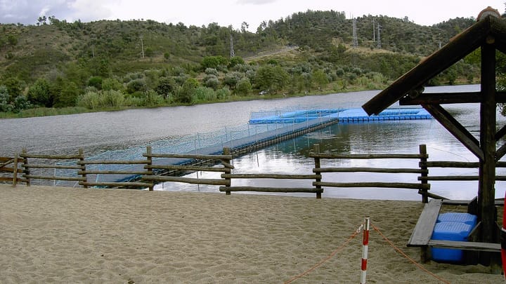 The Tagus at Ortiga's river beach, with sand in the foreground, a wooden fence and floating walkways on the water below wooded hills