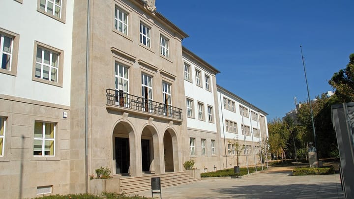 The granite and white facade of the Carolina Michaëlis secondary school in Porto, with arched entrance doors under a balcony, seen on a sunny day