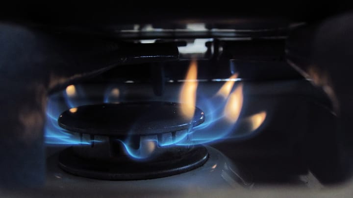 Blue and orange flames around the burner of a domestic gas hob, seen close up in a dim kitchen