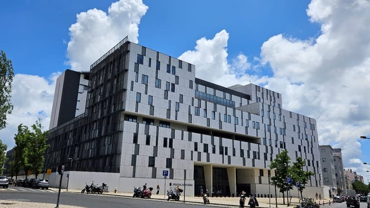 The headquarters of the Policia Judiciaria on Rua Gomes Freire in Lisbon, a large grey and white modern building with motorbikes parked outside under a blue sky
