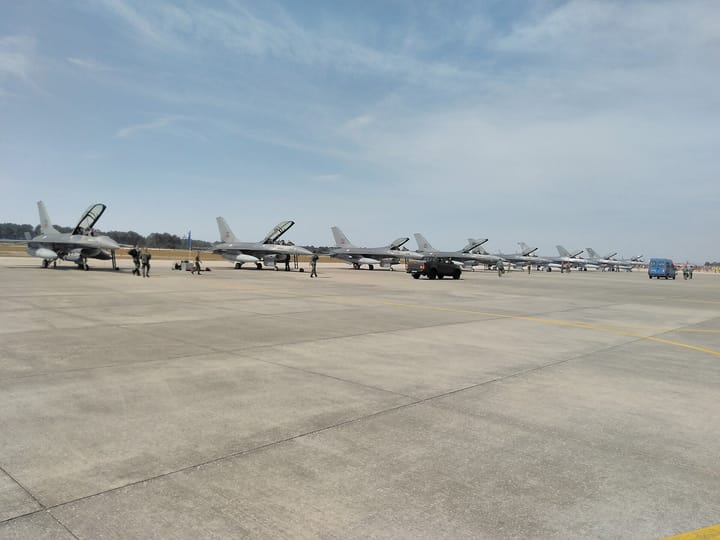 A row of Portuguese Air Force F-16 fighter jets parked on the apron at Monte Real Air Base, with ground crew walking between them under a blue sky