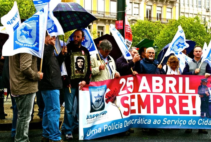 Portuguese police union members marching in Lisbon with ASPP flags overhead and a banner reading 25 Abril Sempre and Uma Policia Democratica ao Servico do Cidadao.