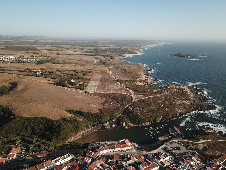 Aerial view of Porto Covo on the Alentejo coast, its small harbour full of boats and the rocky Ilha do Pessegueiro lying offshore.