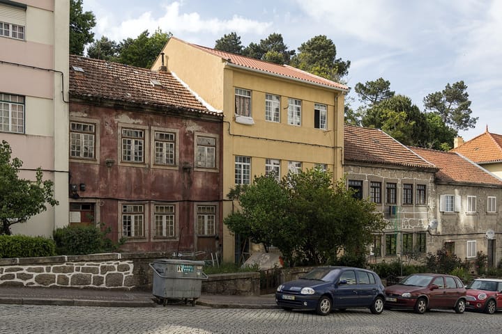 Cars with Portuguese registration plates parked on a cobbled street below old houses in Guarda