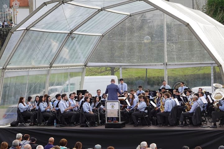 A philharmonic band in blue shirts playing under a glass marquee at a concert in Povoa de Lanhoso, northern Portugal