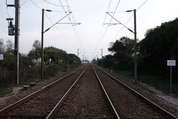 Two tracks of the Linha do Norte running straight into the distance under overhead catenary, with a Portuguese warning sign beside the ballast