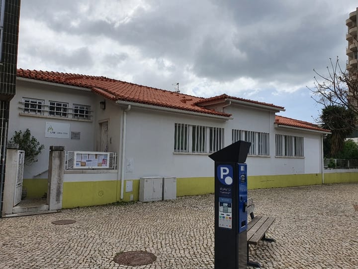 A single-storey white health centre with a terracotta roof and a USF Luisa Todi sign, on a cobbled square in Setúbal