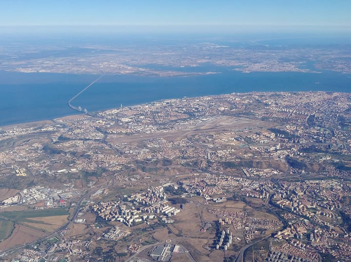 An aerial view of Lisbon showing the runways of Humberto Delgado Airport running through the city, the Tagus estuary, the Vasco da Gama bridge and the Montijo airfield on the far bank.
