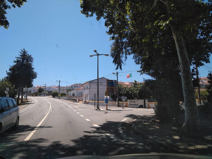 The road into Vila de Arronches, with white houses, plane trees and a Portuguese flag, one of the towns where TAAPedido runs