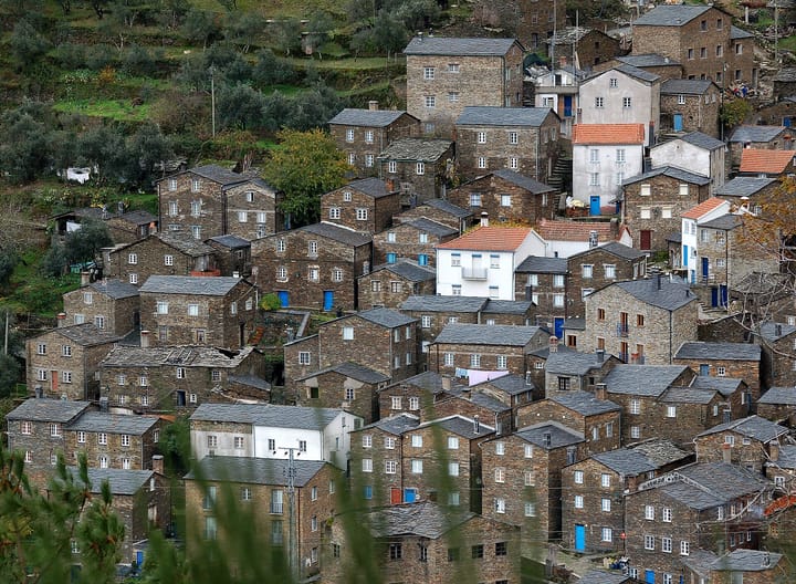 Stone and schist houses packed tightly on a steep hillside in the village of Piódão in central Portugal, with slate roofs, blue painted doors and washing hung out between them.