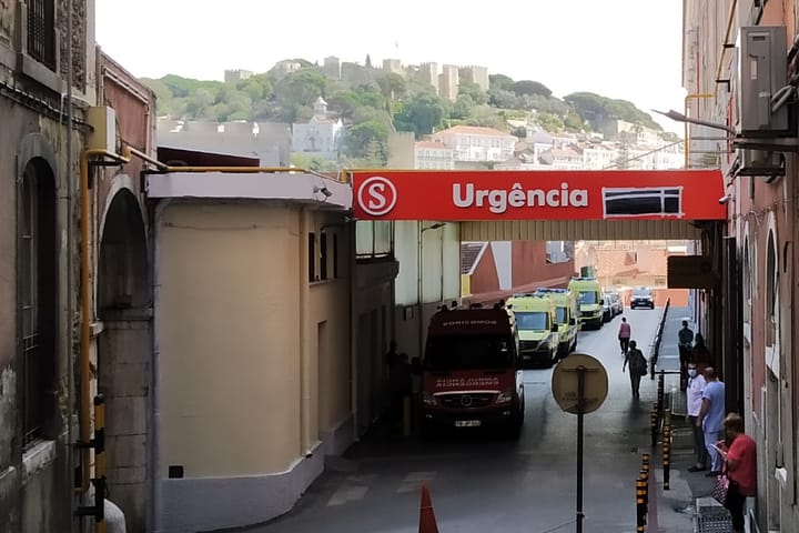 The Urgência entrance of the Hospital de São José in Lisbon, with ambulances queued beneath the red sign and the Castelo de São Jorge on the hill behind