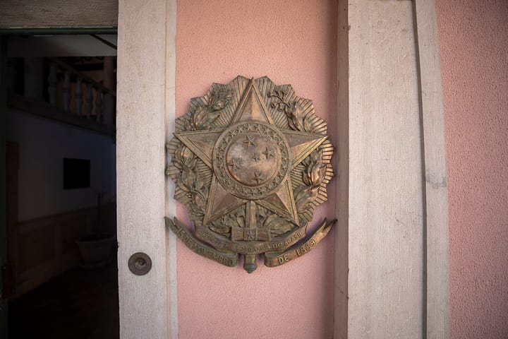 The bronze coat of arms of the Federative Republic of Brazil mounted beside the doorway of the Brazilian Embassy in Lisbon, on a pink rendered wall