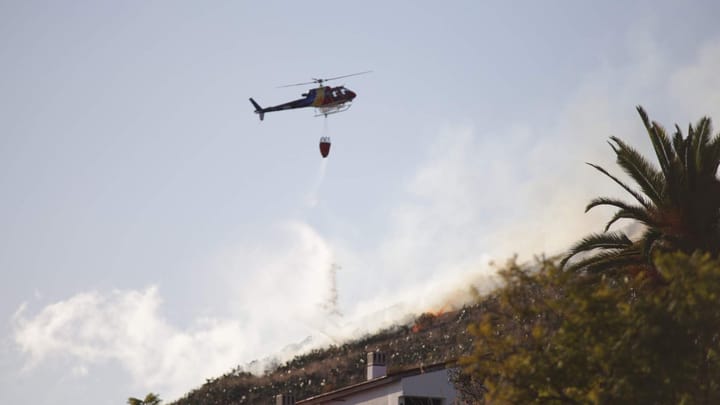 A helicopter drops water from a suspended bucket on a wildfire above houses in Funchal