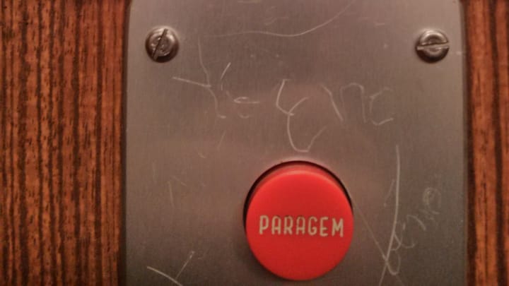 A red emergency stop button marked Paragem on the control panel of a lift in Portugal