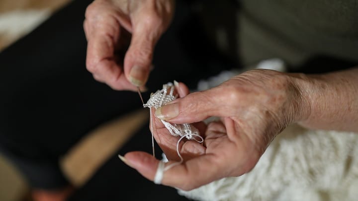 The hands of an older woman crocheting white lace