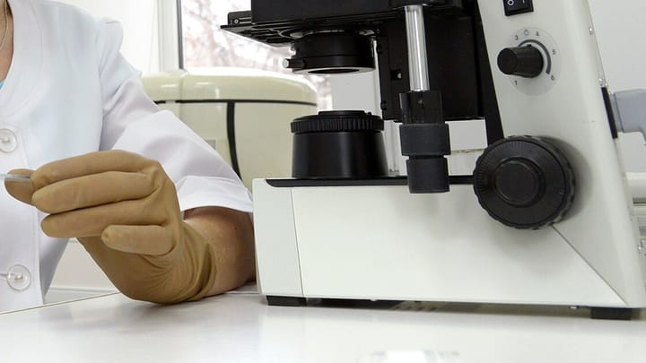 A gloved hand holding a glass slide beside a microscope in an IVF laboratory