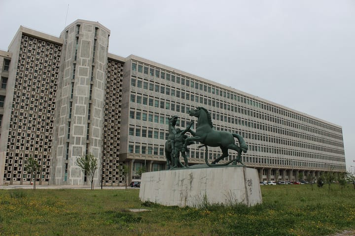 The long modernist facade of the Palacio da Justica courthouse in Lisbon, with a bronze group of two rearing horses and a man on a stone plinth on the grass in front of it