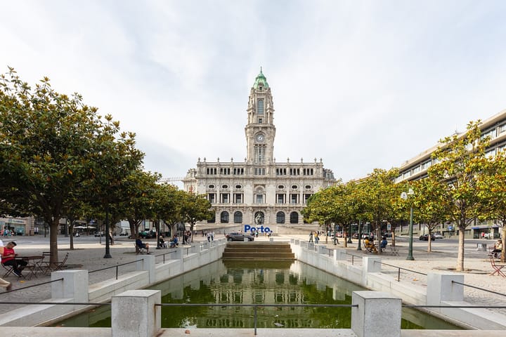 Porto City Hall seen down the length of Avenida dos Aliados, its clock tower above a stone facade, with the reflecting pool and magnolia trees of the square in the foreground.
