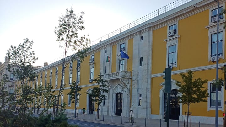 The long yellow and white facade of Portugal's Ministry of Finance on Avenida Infante D. Henrique in Lisbon, with the Portuguese and European Union flags above the marble main entrance