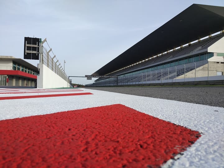 Track-level view along the red and white kerbing of the main straight at the Algarve International Circuit in Portimao, with the empty grandstand and pit wall on either side