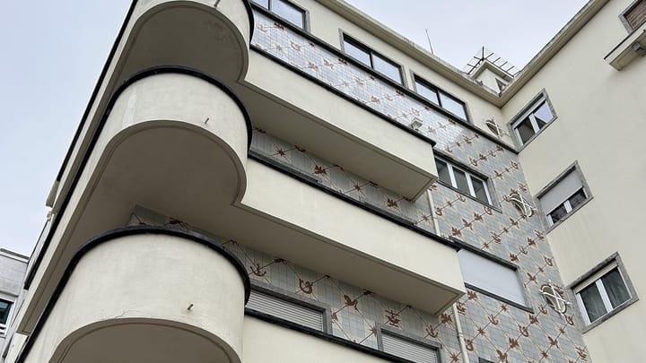 Looking up at the corner of a Lisbon apartment block with curved modernist balconies and a facade of blue and brown patterned azulejo tiles