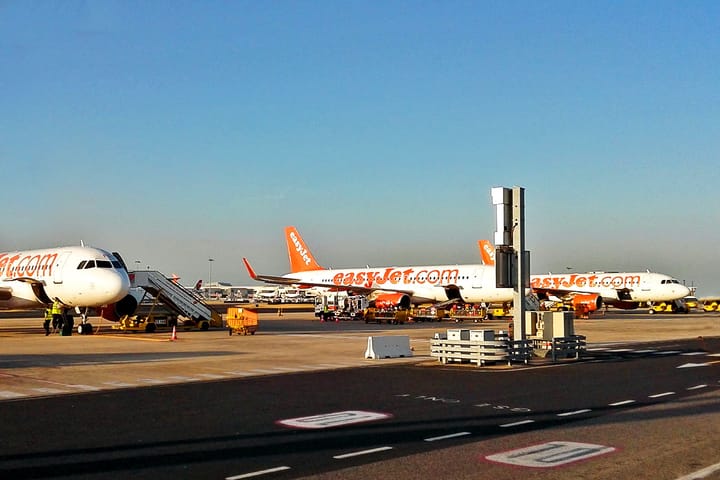Three easyJet aircraft in orange and white livery parked on an airport apron in late afternoon light, with boarding stairs and ground crew in high-visibility jackets