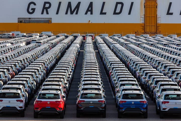 Rows of new Volkswagen T-Roc cars lined up on the quayside at the port of Setubal in Portugal in front of the orange and white hull of a Grimaldi car carrier
