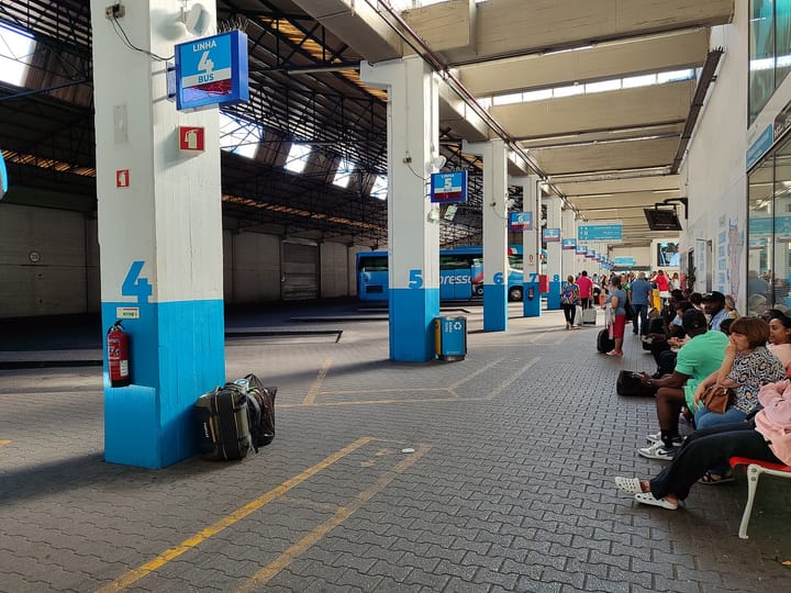 The covered boarding area of Lisbon's Sete Rios coach terminal, with numbered platform pillars marked Linha 4, 5 and 6, a parked coach and passengers waiting on benches