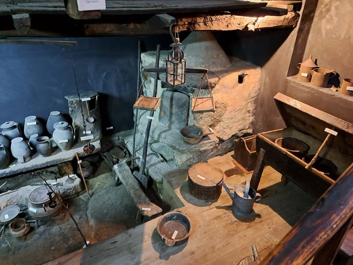 Traditional Portuguese craft objects on display at Mezio in northern Portugal: black clay pots on a stone shelf, hanging scales, tinware and wooden vessels